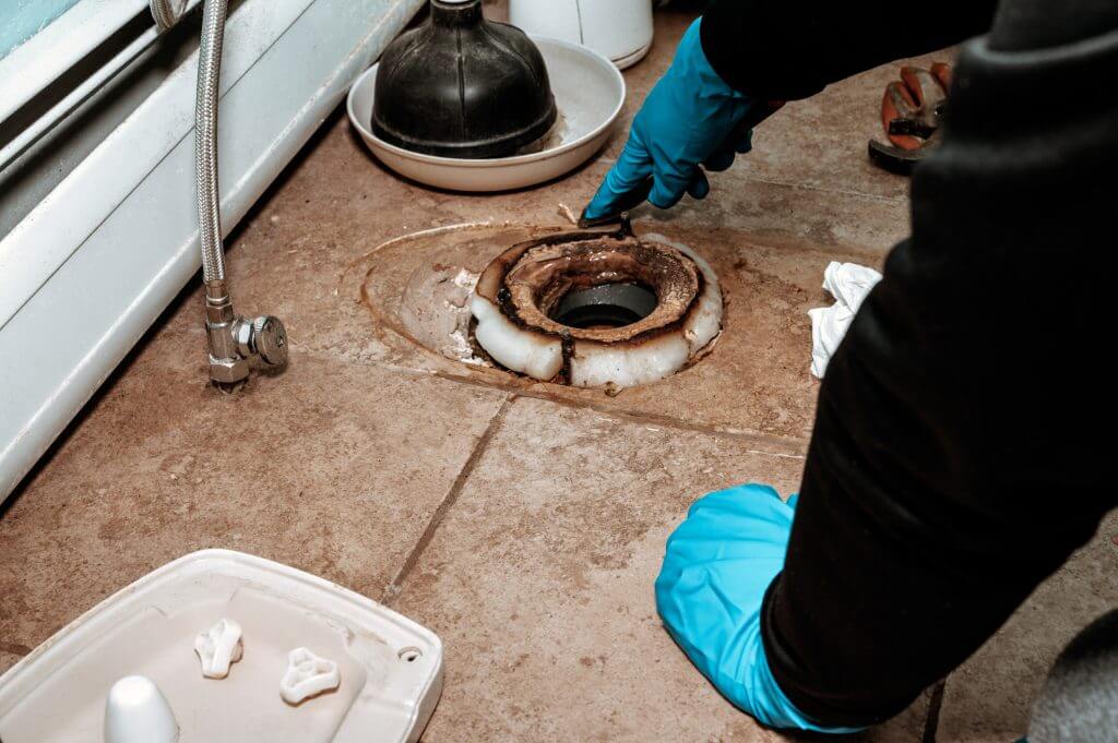 Close-up image showing a plumber replacing the wax ring seal at the base of a toilet.