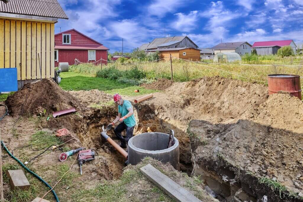Connecting inlet sewer pipe to concrete ring during installation of septic tank, construction worker takes measurements.