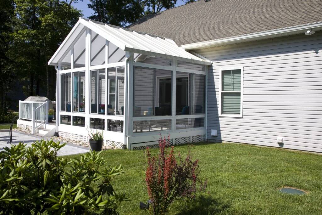 Back yard exterior of home with sun room, patio, and manicured lawn in the suburbs.