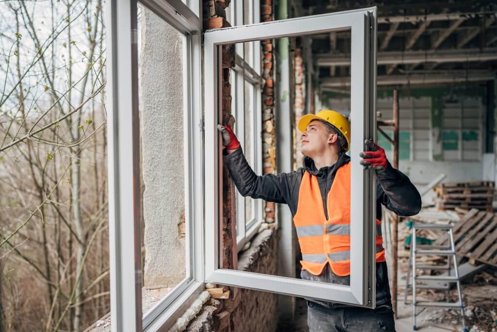 Skilled worker is seen adjusting a new window in the frame of a building under construction