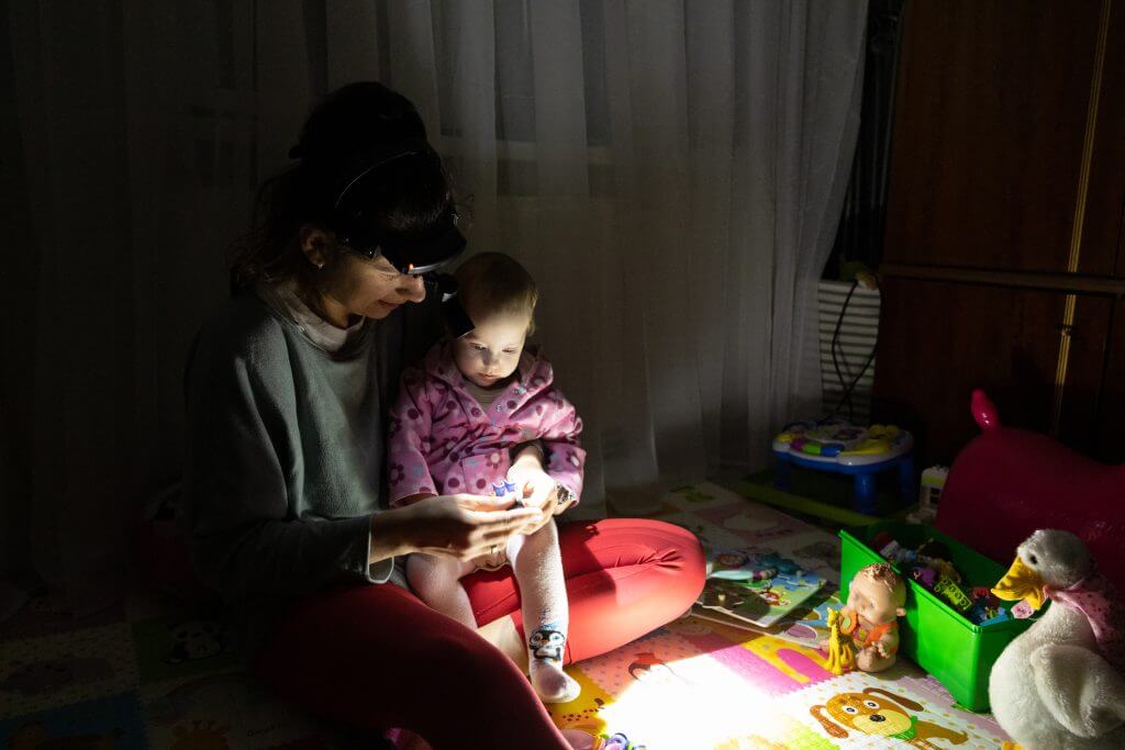 The mother plays with her daughter sitting on the floor with a flashlight in complete darkness due to a blackout.
