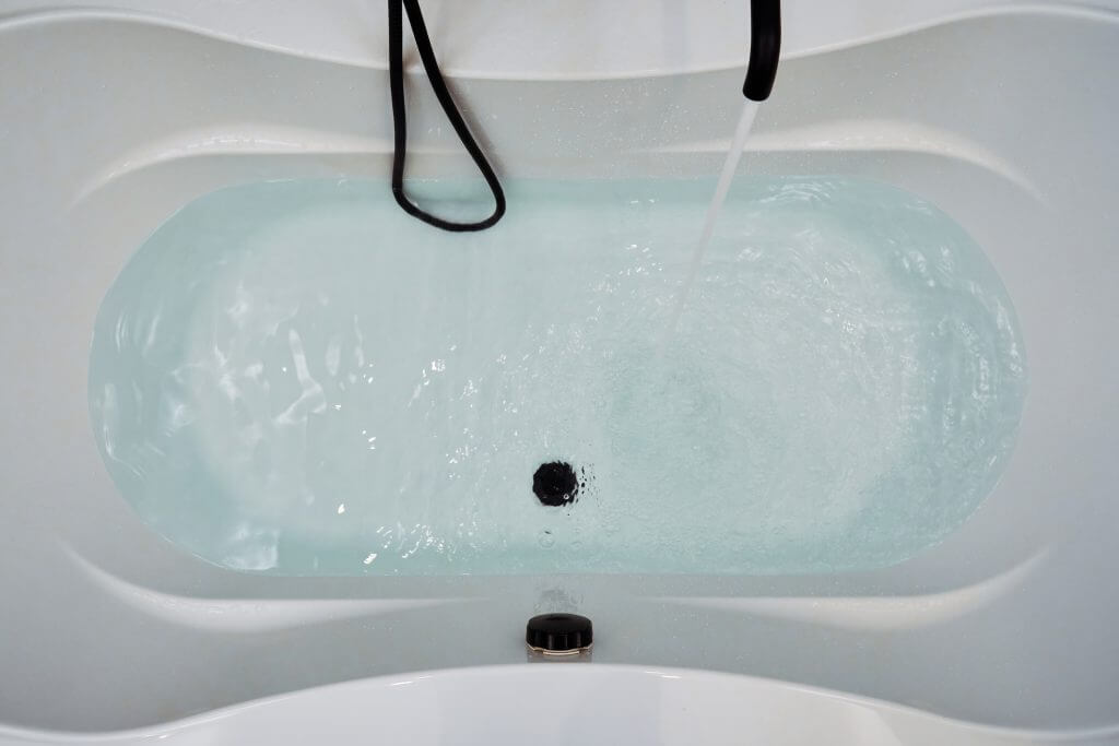 An elegant bathtub is filled with clear blue water from a black faucet. Interior and design backgrounds