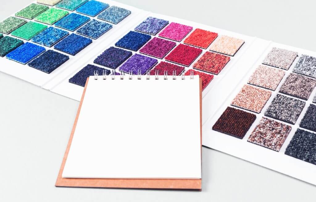 Multicolored carpet swatches catalogue book and notepad on blue desk background. 