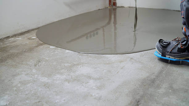 Construction worker is pouring self-leveling concrete mix on the floor to create a smooth and level surface