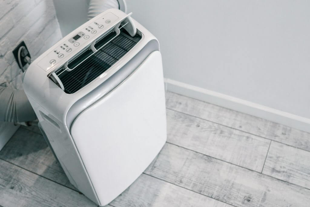 Close-up of a portable air conditioner with digital display and control panel, placed on a wooden floor near a wall socket.