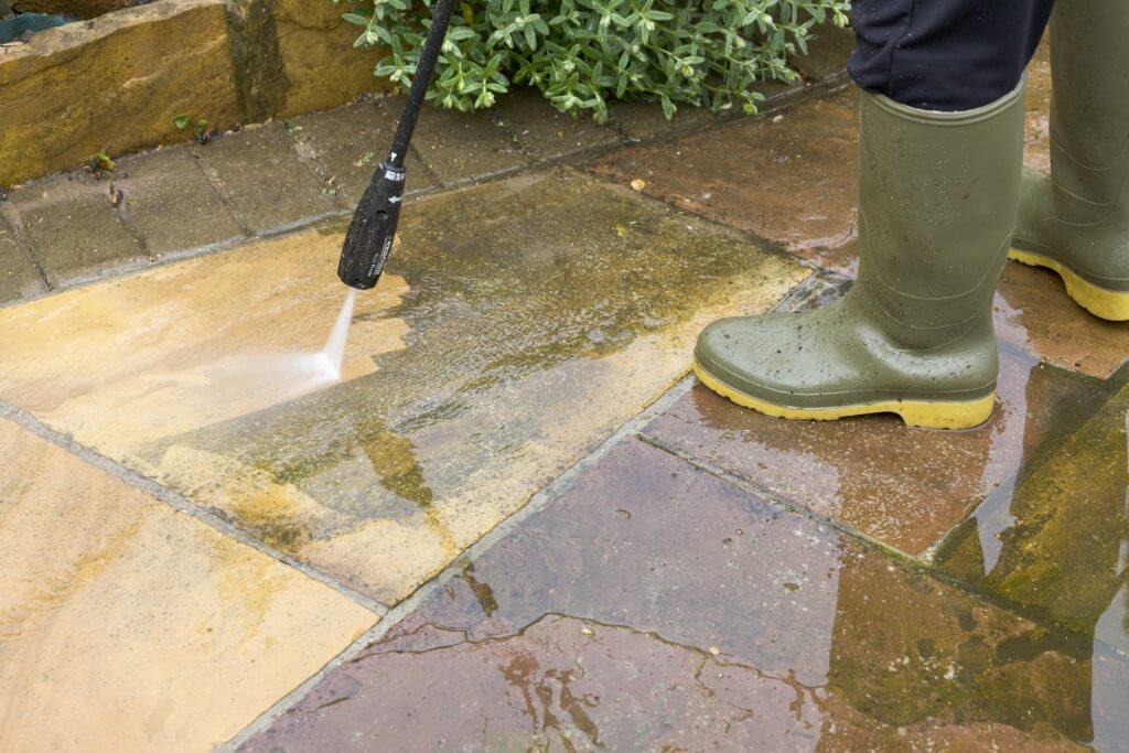 Man wearing wellingtons jet washing Indian Sandstone patio