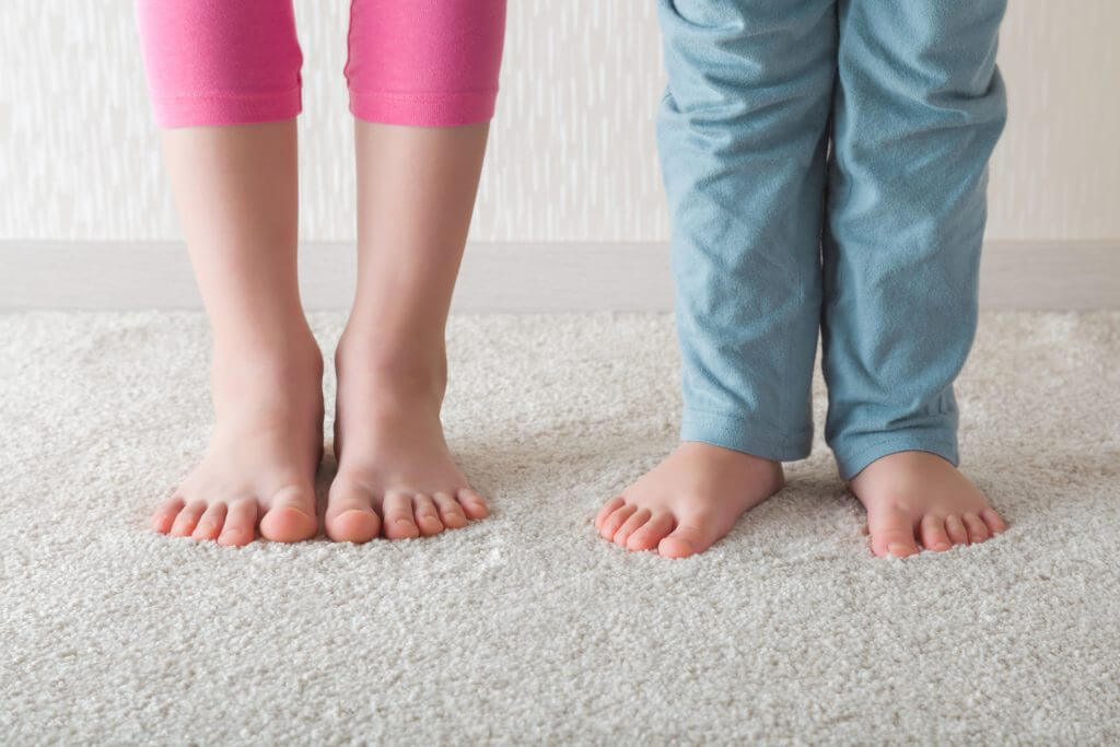 Two toddlers standing on beige soft home carpet. 